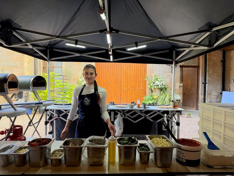 Scottish Pizza Co pop-up pizza station under a gazebo, with a chef ready behind a row of topping tubs