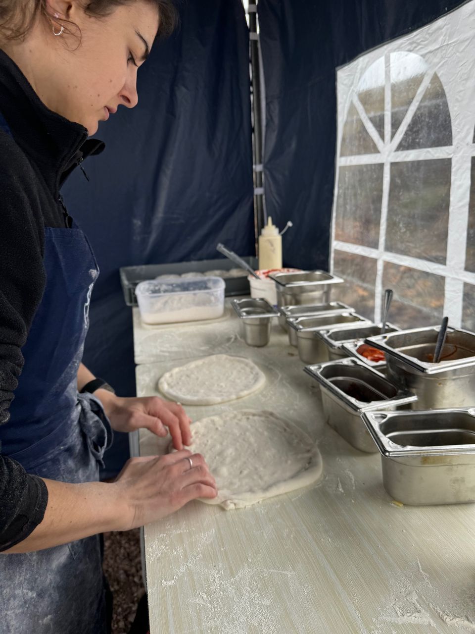 Scottish Pizza Co chef stretching fresh pizza bases by hand on a floured counter inside our pop-up gazebo