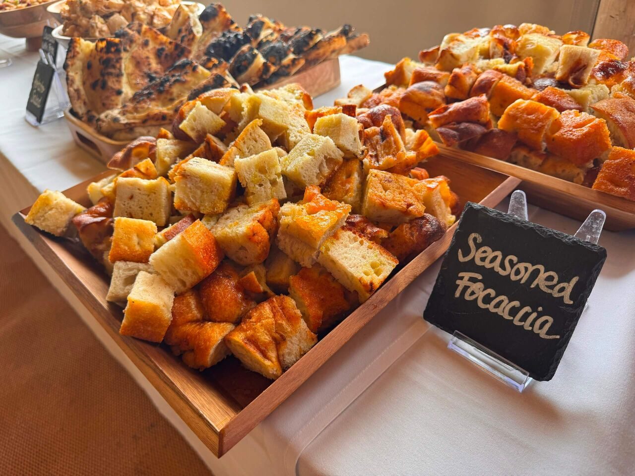 Seasoned focaccia squares on a wooden board with a chalkboard label